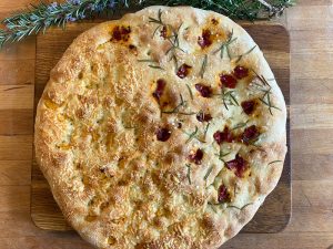 Ganzes Focaccia halb mit Käse und halb mit getrockneten Tomaten und Rosmarin