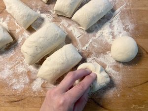 Pizzateig in gleiche Portionen eingeteilt. Schritt des Rundformens wird gezeigt.