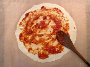 Fertig ausgerollter Pizzateig mit Pizzasauce bestrichen.
