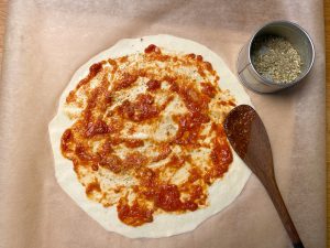 Fertiger, dünn ausgerollter Pizzateig wird mit Pizzasauce bestrichen.