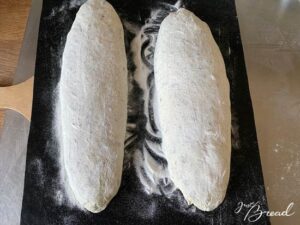 Brotstangen aus dem Bäckerleinen auf ein Backpapier legen