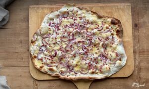 Frisch gebackener Flammkuchen mit knusprigem Sauerteigboden aus Weizen-Anstellgut, belegt mit Schmand, Schinkenwürfeln und Gruyère-Käse.