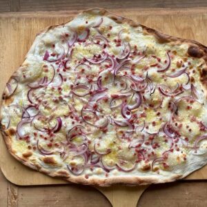 Frisch gebackener Flammkuchen mit knusprigem Sauerteigboden aus Weizen-Anstellgut, belegt mit Schmand, Schinkenwürfeln und Gruyère-Käse.