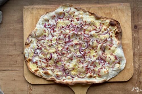 Frisch gebackener Flammkuchen mit knusprigem Sauerteigboden aus Weizen-Anstellgut, belegt mit Schmand, Schinkenwürfeln und Gruyère-Käse.