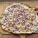 Frisch gebackener Flammkuchen mit knusprigem Sauerteigboden aus Weizen-Anstellgut, belegt mit Schmand, Schinkenwürfeln und Gruyère-Käse.