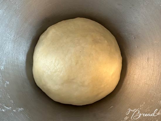 Flammkuchenteig zu einer Kugel geformt, mit Öl bestrichen und abgedeckt zum Ruhen bereit.