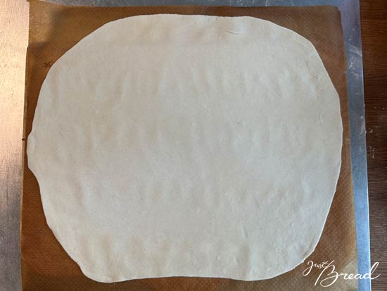 Dünn ausgerollter Flammkuchenteig auf Backpapier