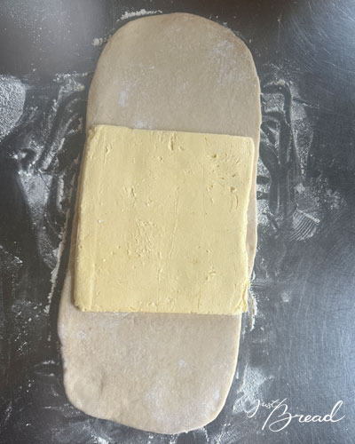 Rechteckige Butterplatte liegt mittig auf ausgerolltem Teig für die Laminierung des Schoko-Croissant-Toast.