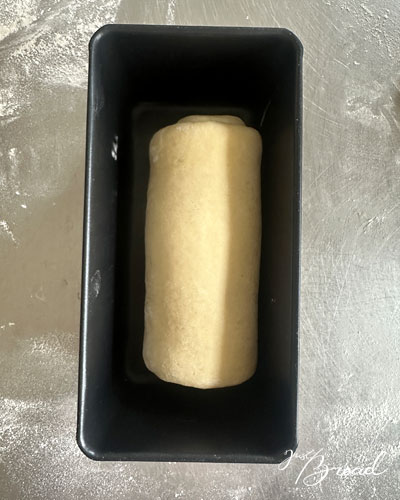 Aufgerollter Teigling liegt mittig in einer Kastenform vor der Stückgare.