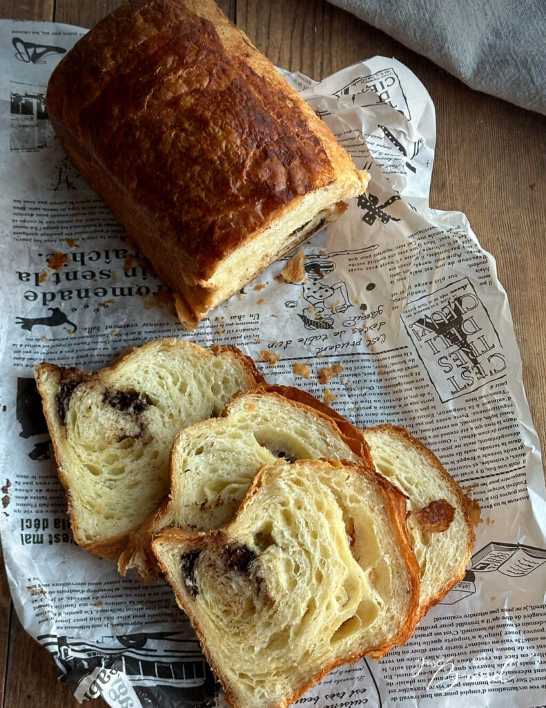 Mehrere Scheiben Schoko-Croissant-Toast mit blättriger Krume und schokoladigem Kern auf rustikalem Papier.