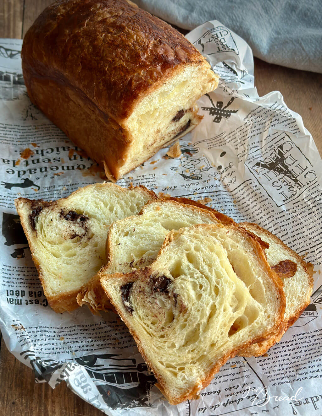 Angeschnittener Schoko-Croissant-Toast mit zarter, blättriger Krume und eingewickelter Schokolade auf Papier serviert.