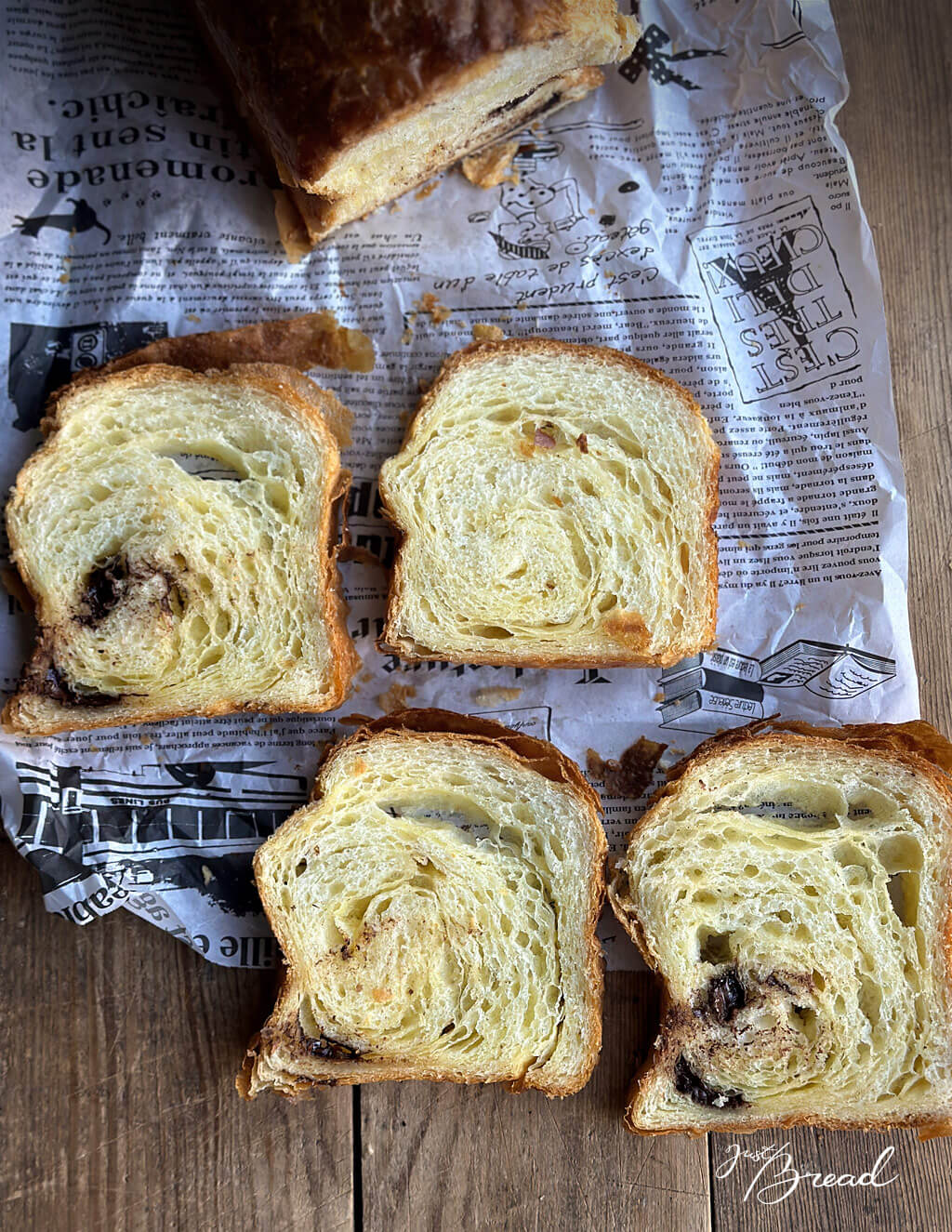 Mehrere Scheiben Schoko-Croissant-Toast mit blättriger Krume und schokoladigem Kern auf rustikalem Papier.