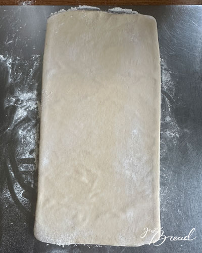 Eingeschlagener Croissantteig wird zu einem langen Rechteck für die erste einfache Tour ausgerollt.