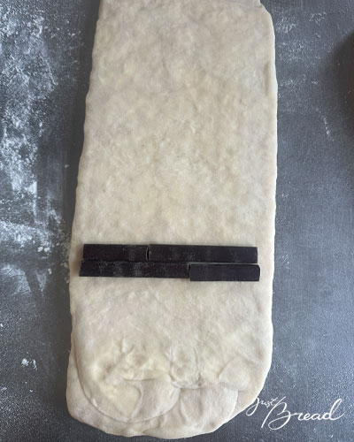 Zwei doppelte Reihen Schokosticks liegen quer auf dem unteren Drittel des tourierten Teigs.