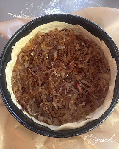 Gedünstete Zwiebeln mit Speck in der Springform auf dem Hefeteig verteilt